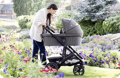 Maminka se usmívá na miminko v kočárku Joie Vinca s korbou Ramble XL na zahradě.