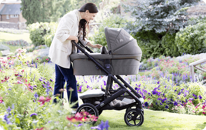 Maminka se usmívá na miminko v kočárku Joie Vinca s korbou Ramble XL na zahradě.