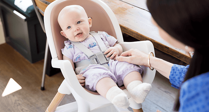 Baby sitting in a brown and white Joie chestnut highchair, looking to the left.