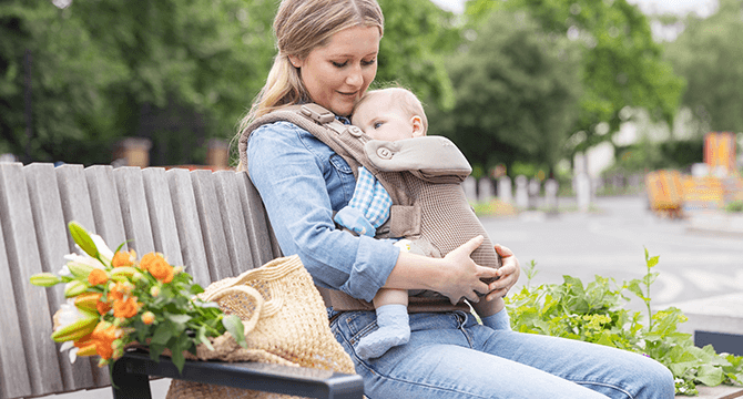 Mum cuddling baby in a mustard yellow Joie Savvy air baby carrier
