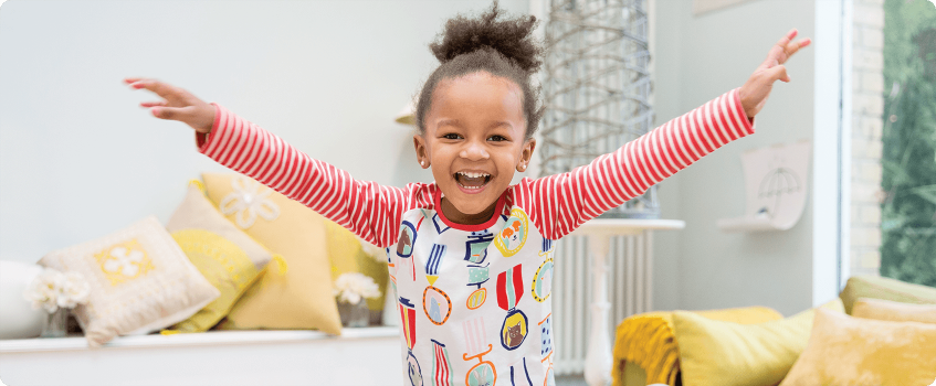 A young girl in a living room throwing her hands in the air and laughing