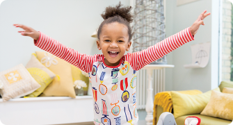 A young girl in a living room throwing her hands in the air and laughing