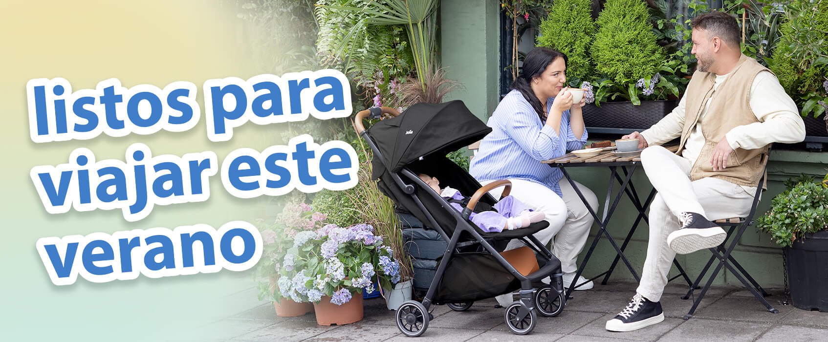 Padres charlando tomando caf&eacute; en una mesa de cafeter&iacute;a en un jard&iacute;n al aire libre. El beb&eacute; est&aacute; relajado c&oacute;modamente a su lado en el cochecito Joie pact pro. El texto en la imagen destaca los imprescindibles para viajar en verano.