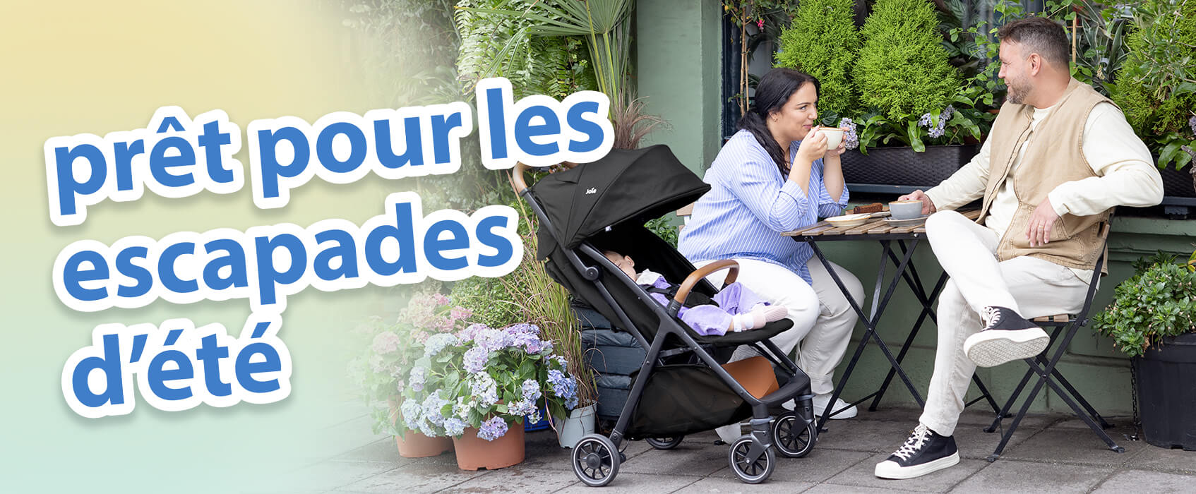 Des parents discutent autour d&rsquo;un caf&eacute; &agrave; une table en terrasse, dans un jardin. B&eacute;b&eacute; se d&eacute;tend confortablement &agrave; c&ocirc;t&eacute; d&rsquo;eux dans la poussette Joie pact pro. Le texte &agrave; l&rsquo;&eacute;cran met en avant les indispensables pour voyager en &eacute;t&eacute;.
