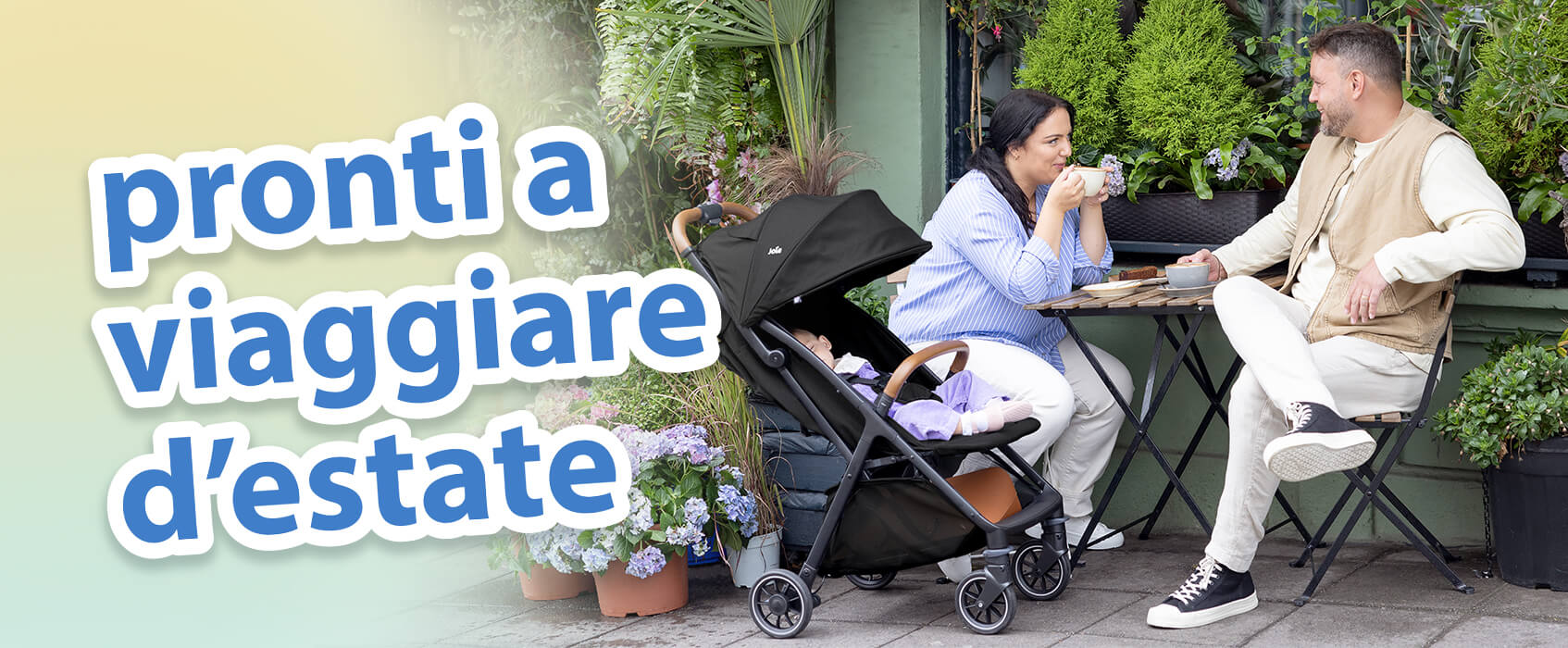 Genitori che chiacchierano davanti a un caff&egrave; a un tavolino in un giardino all&rsquo;aperto. Il bambino si rilassa comodamente accanto a loro nel passeggino Joie pact pro. Il testo sull&rsquo;immagine mette in evidenza gli essenziali per i viaggi estivi.
