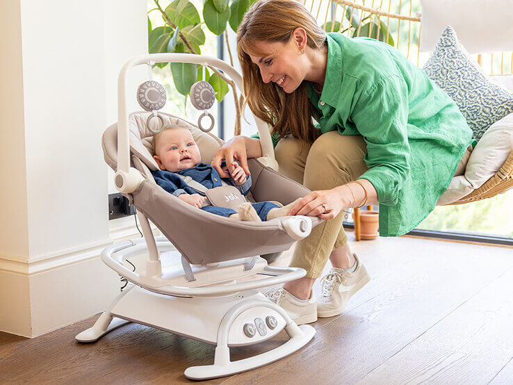 Mom sitting with baby laying in cinnamon 2-in-1 glider and rocker.