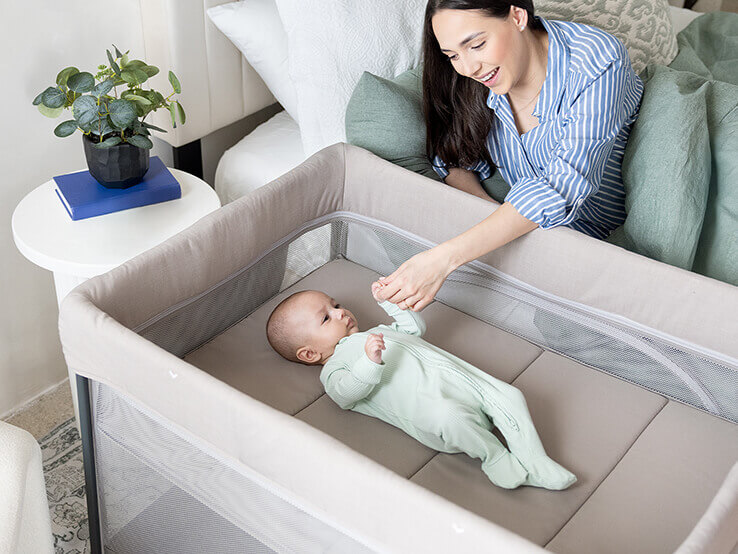 Mom watching baby laying flat on zip-on bassinet of sesame lx in dove at home