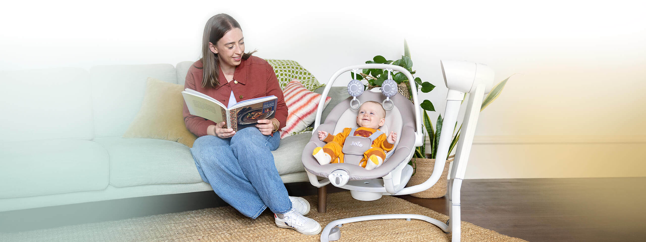 Mom reading a book on the couch while sitting with baby secured in miso 2-in-1 swing and rocker at home