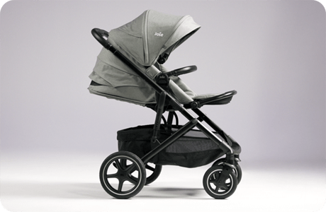 Joie elara Kinderwagen in Grau, in der Seitenansicht nach rechts ausgerichtet, vor violettem Hintergrund.