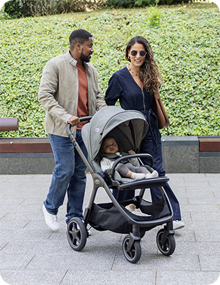 Couple strolling through a park setting, pushing the Joie Signature finiti pushchair in grey with baby comfortably riding in the world facing position.