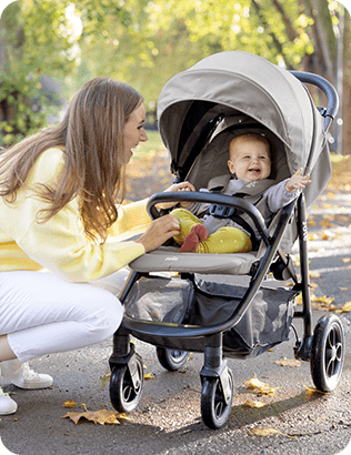 Matka se usmívá a klečí vedle miminka v kočárku Joie Litetrax Pro venku.