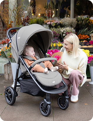 Mother kneels beside baby sitting comfortably in gray Joie Litetrax pushchair.