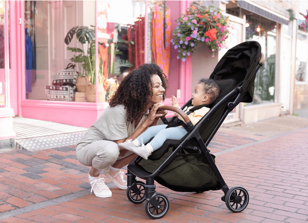 Eine Mutter beugt sich zu ihrem lachenden Kind in einem Joie Kinderwagen.